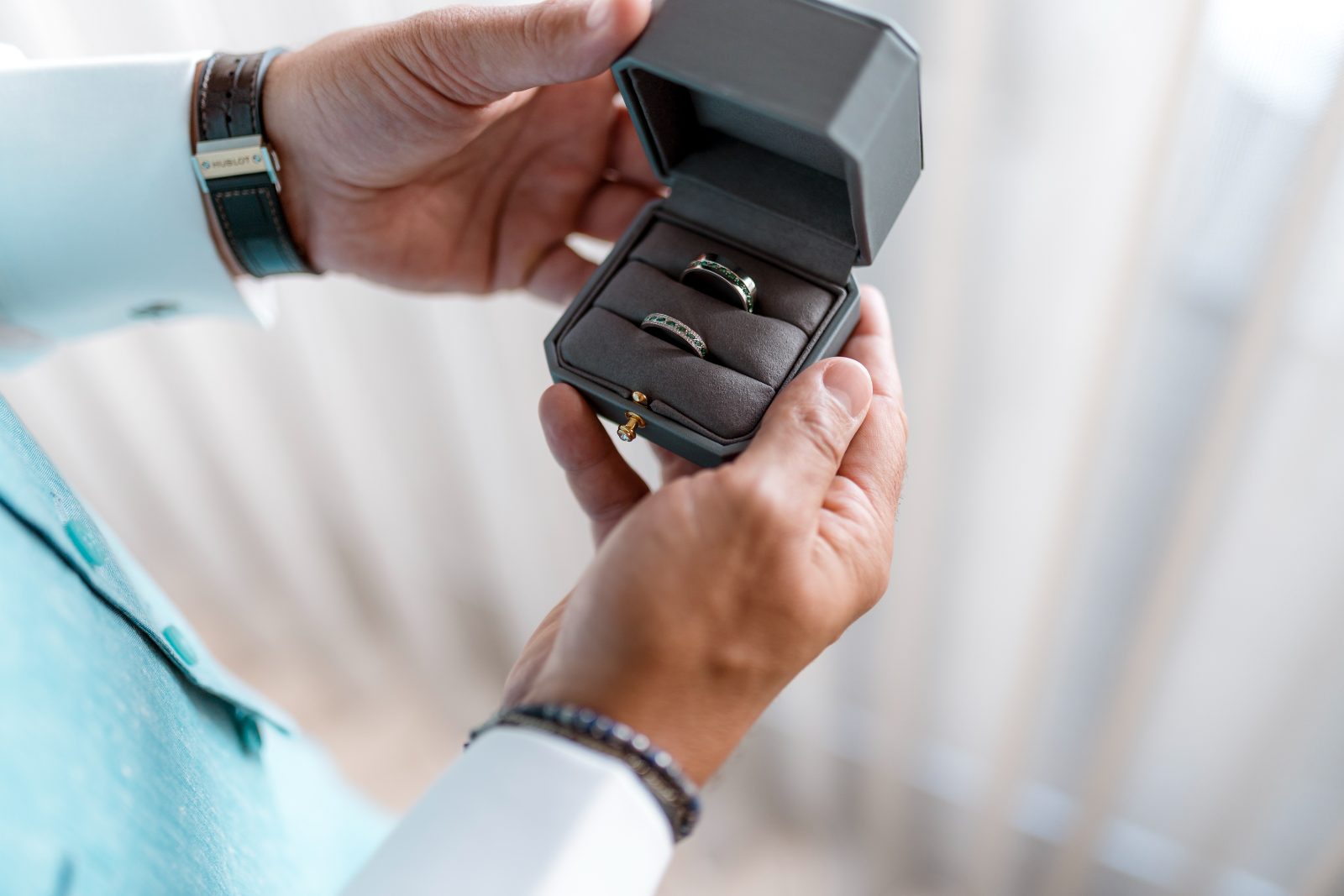 Two wedding rings are displayed in a box held by a man, set inside the Avila Beach Hotel