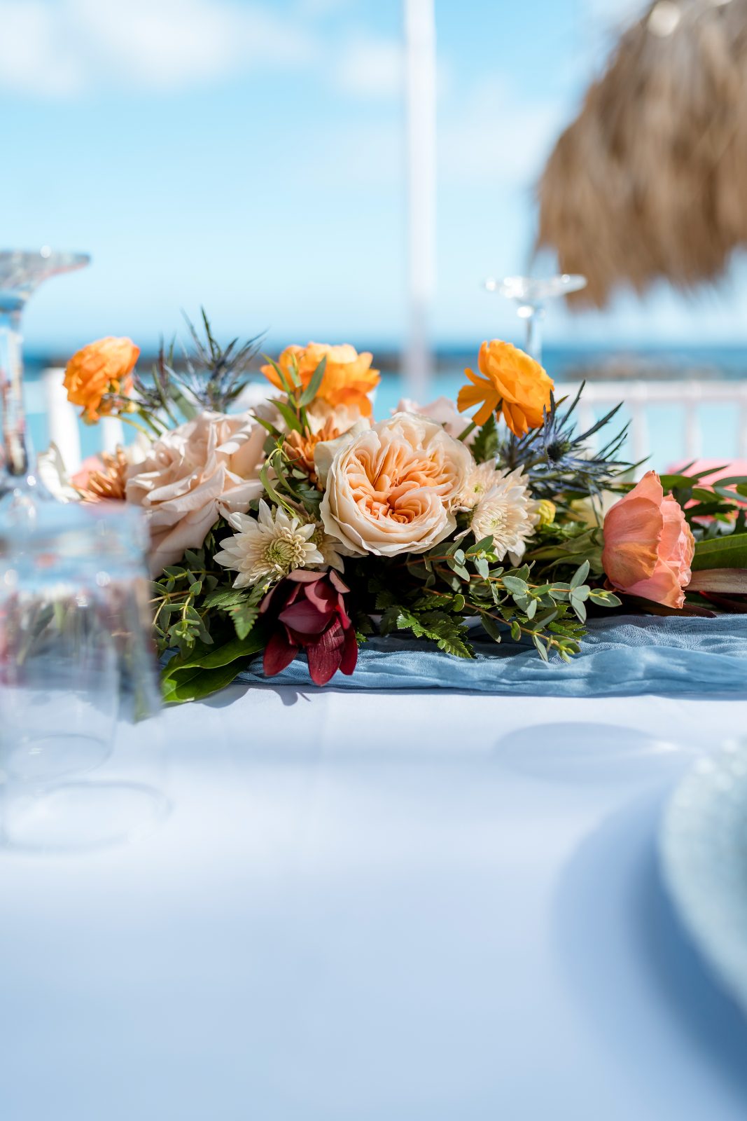 The wedding setup features a floral centerpiece on a table, set outdoors at the Avila Beach Hotel, with the ocean visible in the background