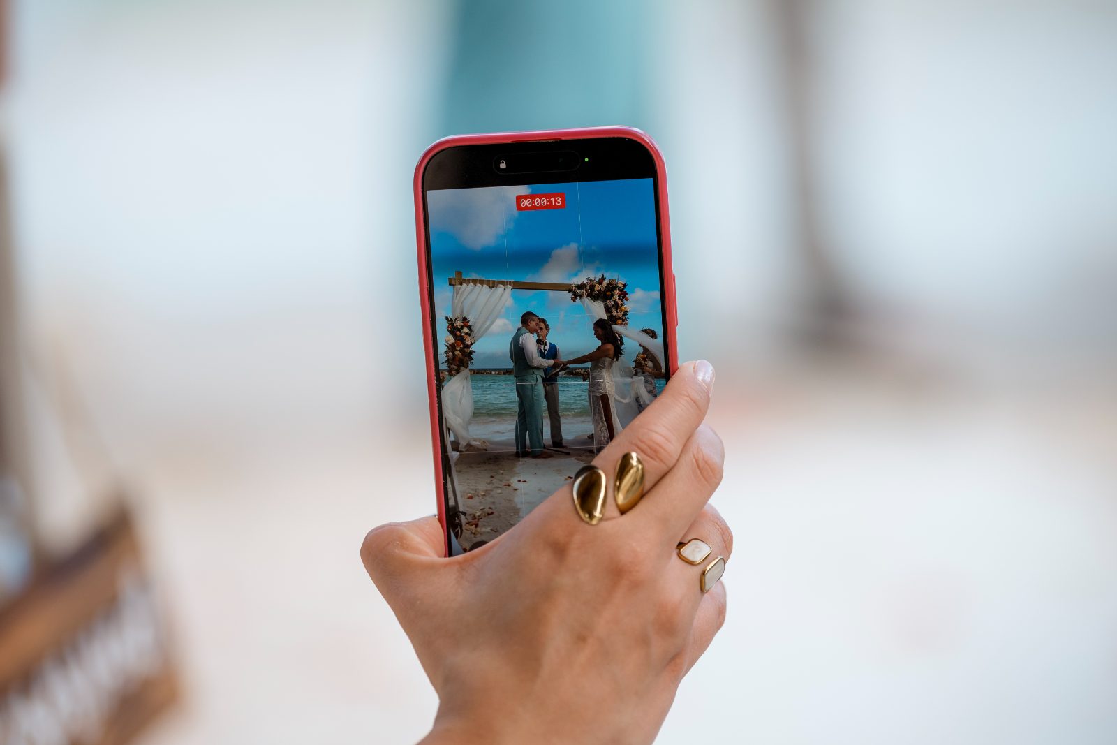A smartphone displays Anika and Sarne exchanging vows at their wedding on the beach outside the Avila Beach Hotel