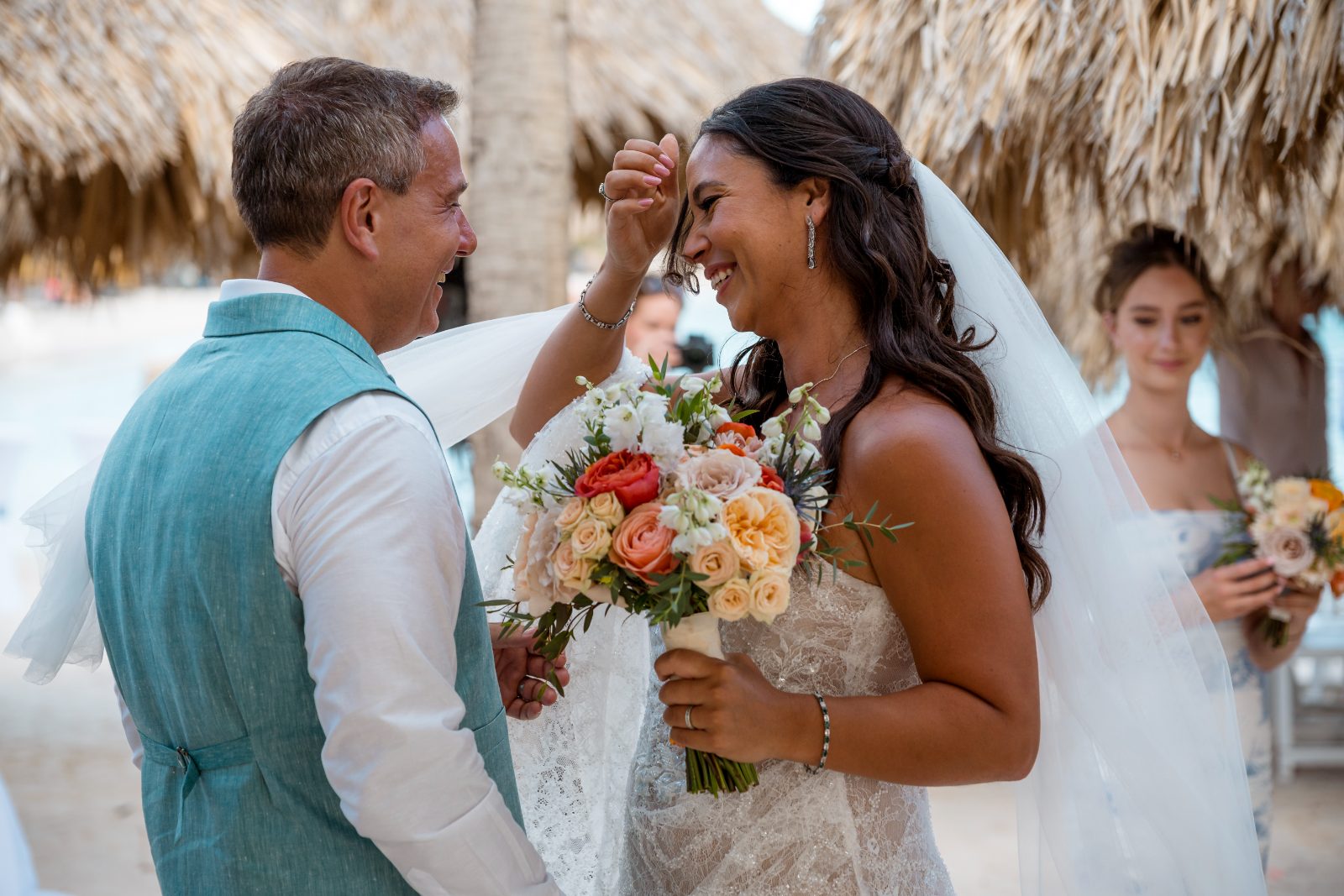 Anika and Sarne are exchanging vows at their wedding ceremony at Avila Beach Hotel, with a floral bouquet and guests nearby