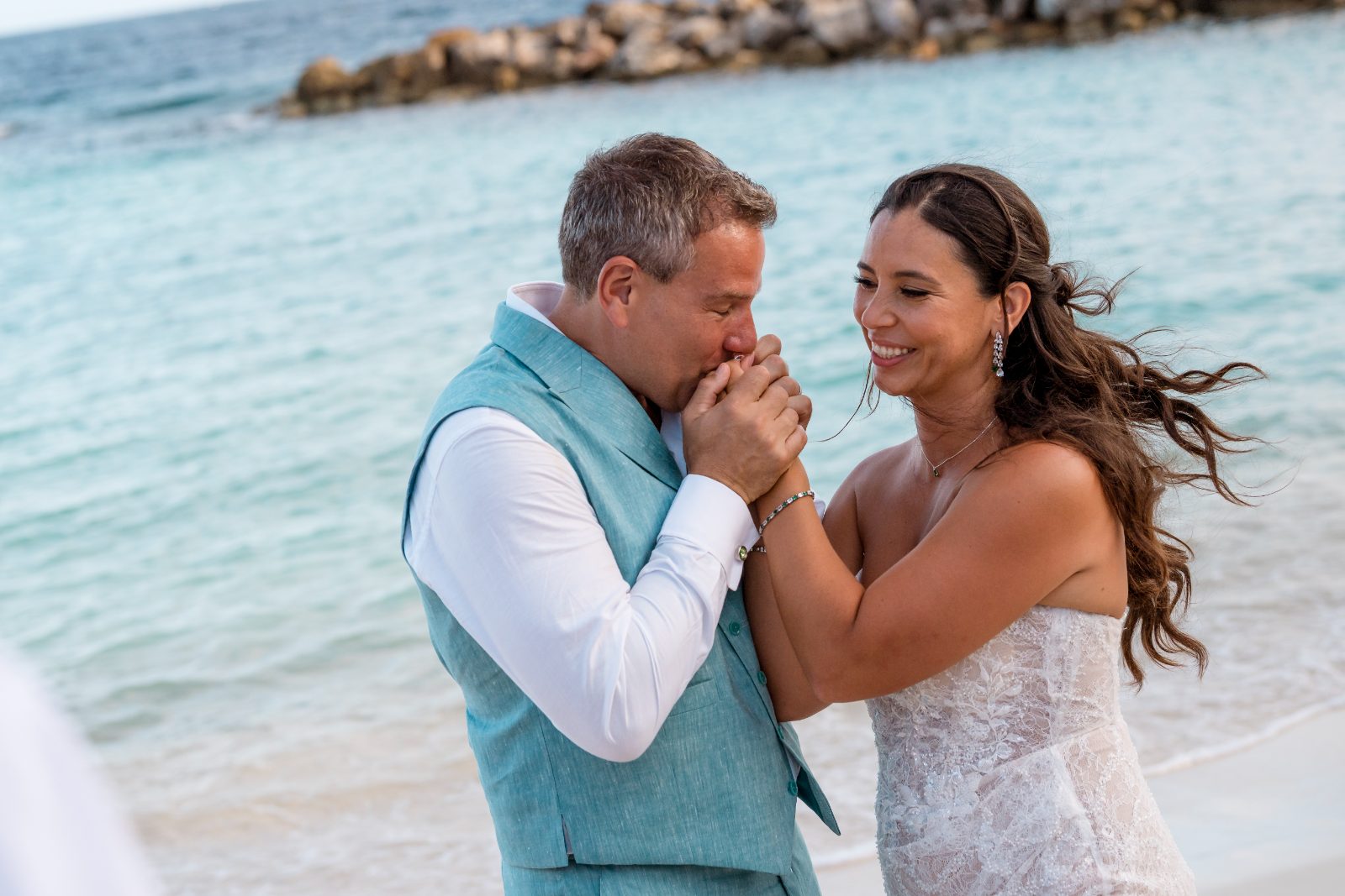 Anika and Sarne stand on the beach at Avila Beach Hotel, smiling and holding each other's hands near the water