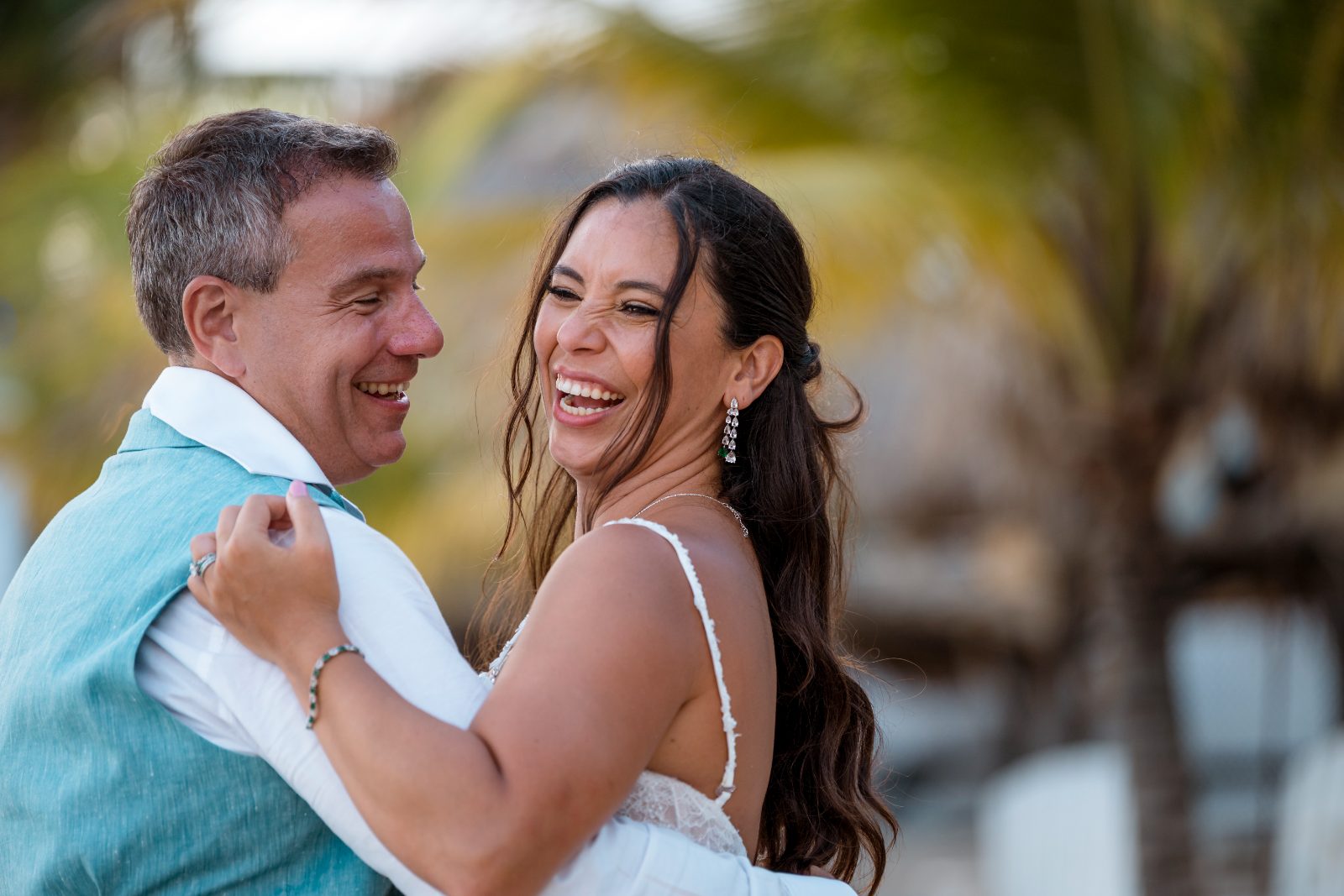 Anika and Sarne are smiling at each other while embracing outdoors at the Avila Beach Hotel, surrounded by palm trees