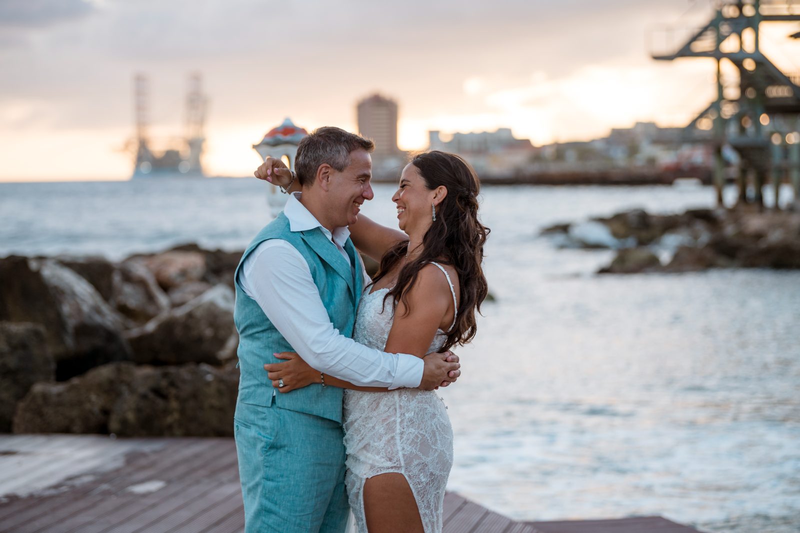 Anika and Sarne are standing by the water at Avila Beach Hotel, smiling and embracing each other during their wedding ceremony