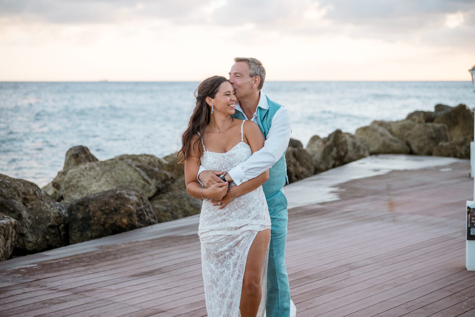 Anika and Sarne are embracing on a wooden walkway by the ocean at Avila Beach Hotel during their wedding
