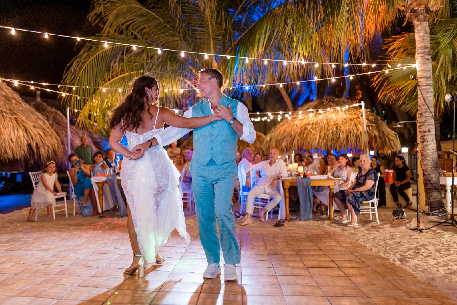Anika and Sarne are dancing on a beachside dance floor at Avila Beach Hotel, with guests seated around them under string lights and palm trees