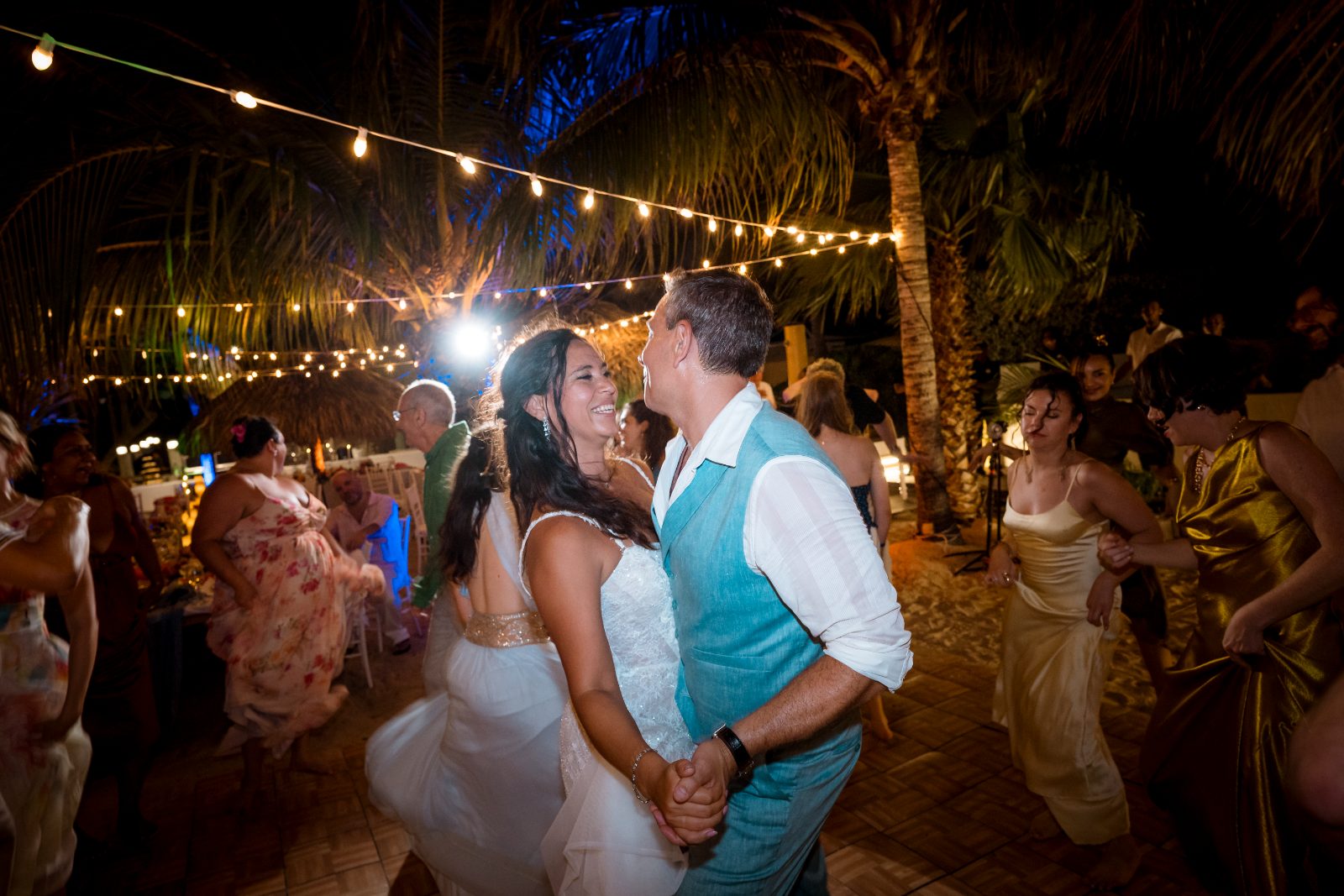 Anika and Sarne are dancing together at their wedding reception outdoors at Avila Beach Hotel, surrounded by guests and string lights