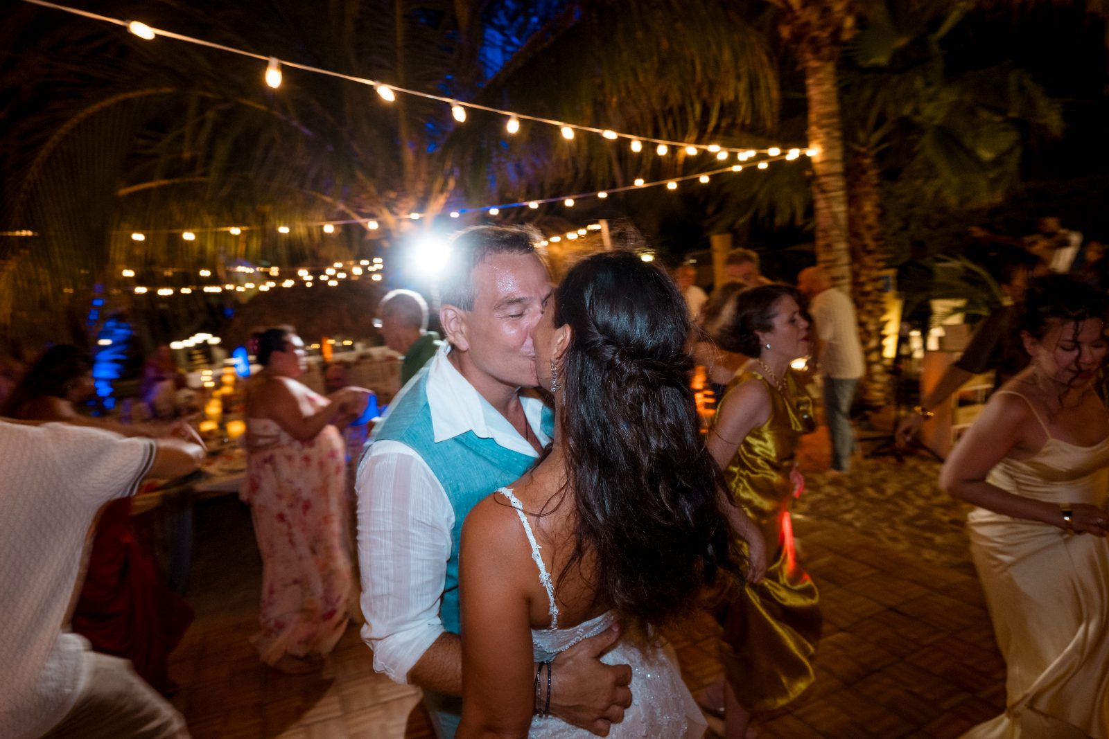 Anika and Sarne are dancing close together at their wedding reception, surrounded by guests and string lights at Avila Beach Hotel