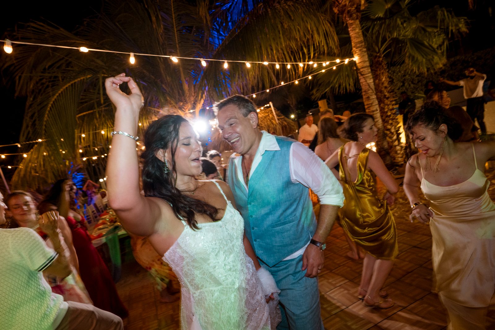 Anika and Sarne dance at their wedding reception, surrounded by guests, under string lights at the Avila Beach Hotel