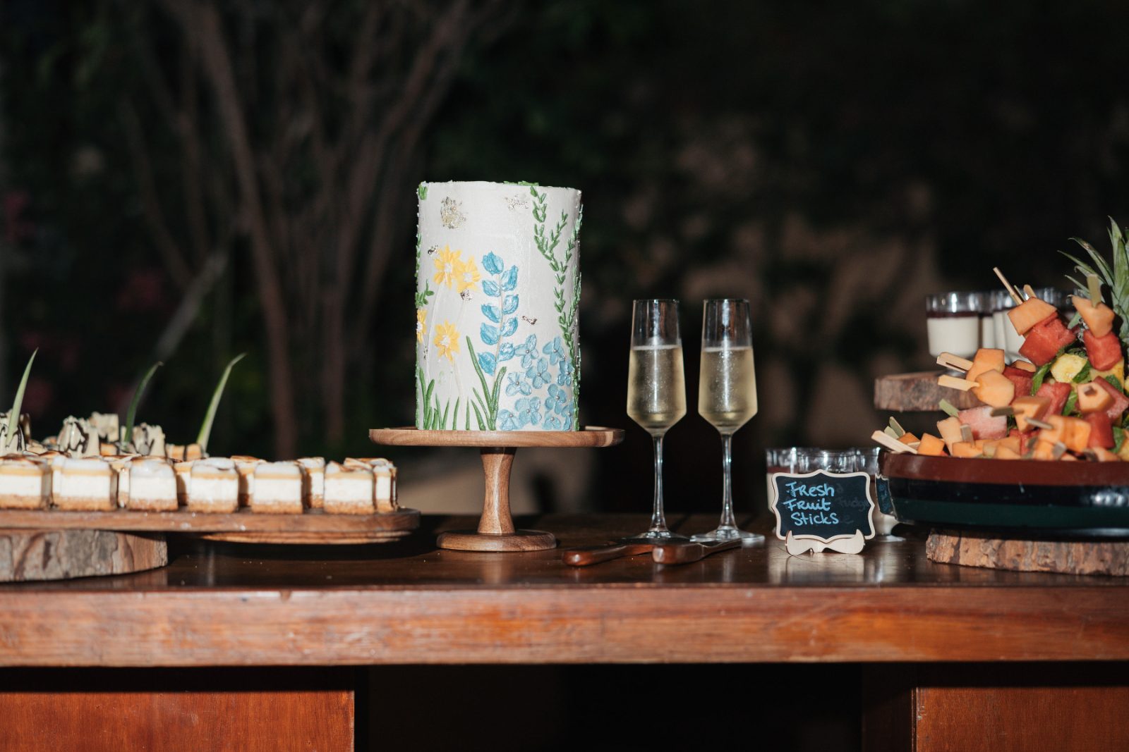 Cailey and Noel's wedding reception at Avila Beach Hotel showcases a decorative cake and various desserts alongside champagne flutes and fresh fruit displays