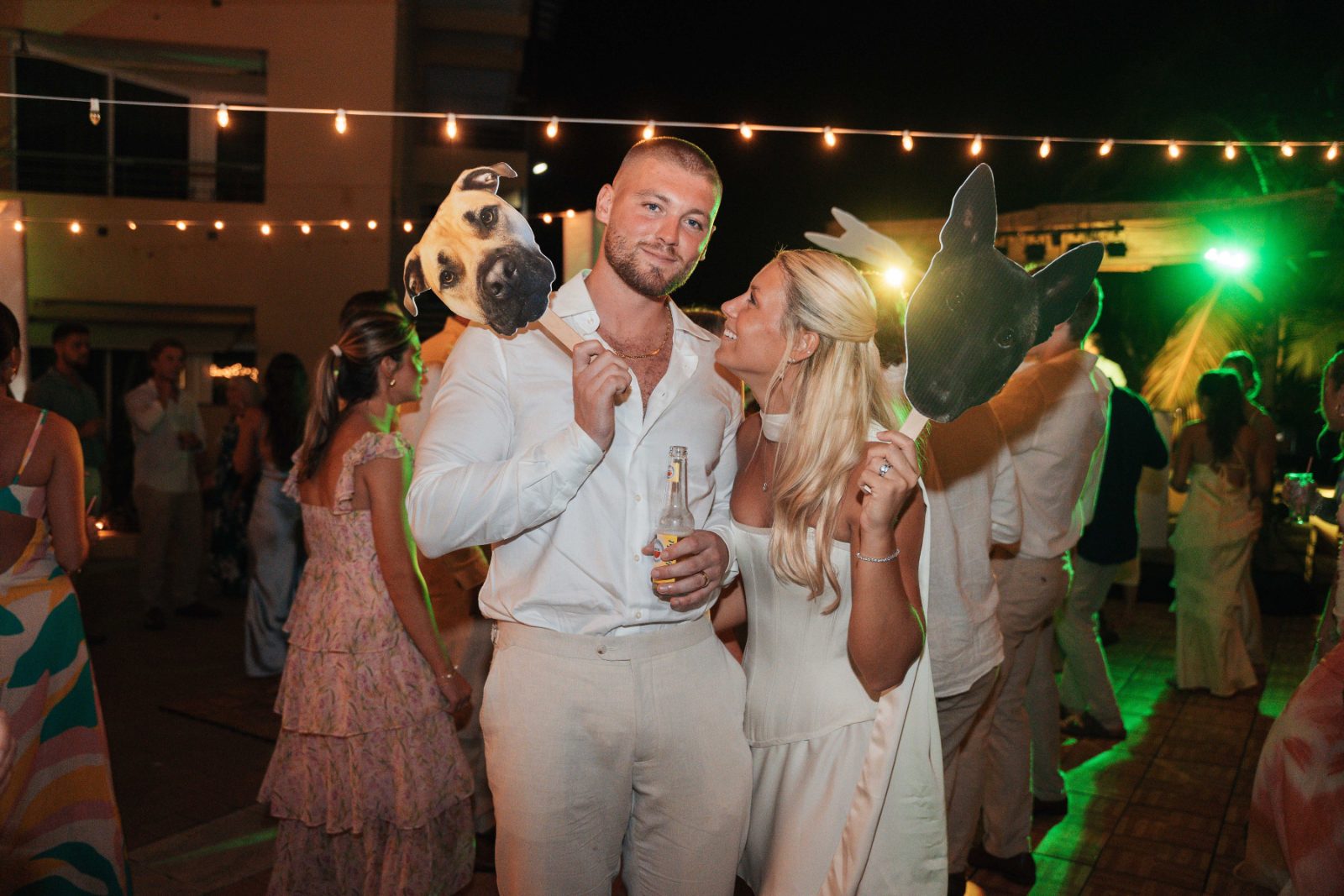 Cailey and Noel celebrate their wedding at Avila Beach Hotel in Curaçao, surrounded by guests, holding masks, with lights strung above them