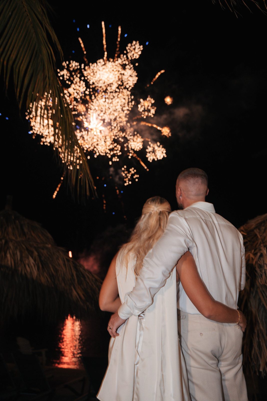 Cailey and Noel stand together by the water at Avila Beach Hotel in Curaçao, watching fireworks explode in the night sky