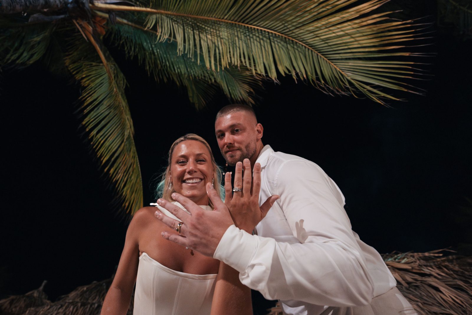 Cailey and Noel show their wedding rings at the Avila Beach Hotel in Curaçao, with palm leaves visible in the background