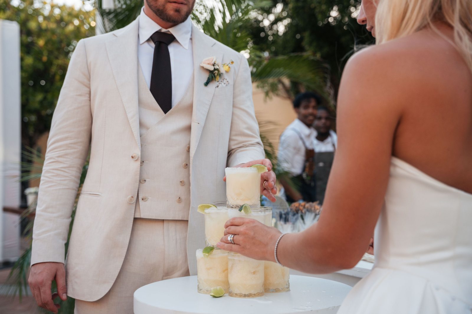 Cailey and Noel are at their wedding reception in Avila Beach Hotel, Curaçao, stacking cocktails on a table while guests look on