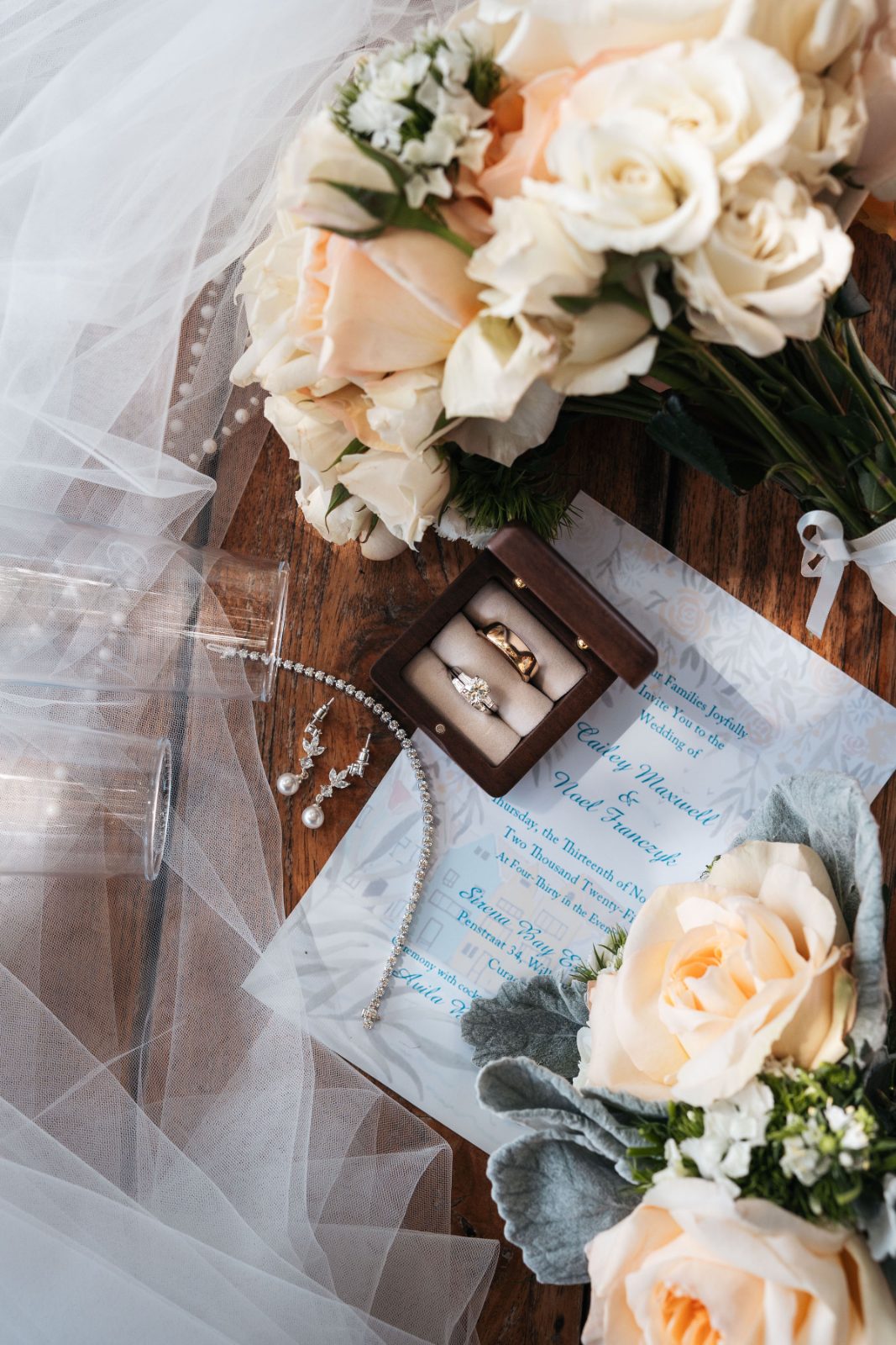 Cailey and Noel's wedding details are displayed on a table, featuring flowers, rings in a box, and a wedding invitation at Avila Beach Hotel, Curaçao