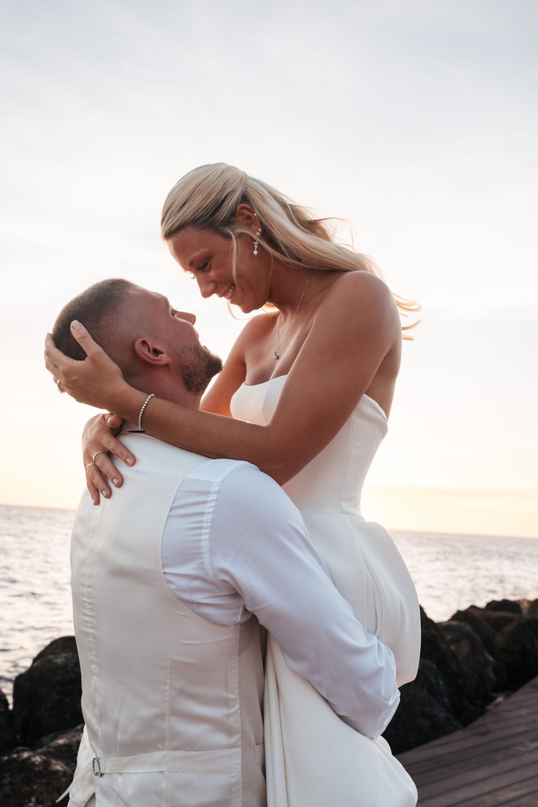 Cailey and Noel pose together on a rocky shore at Avila Beach Hotel in Curaçao during their wedding, with the ocean in the background