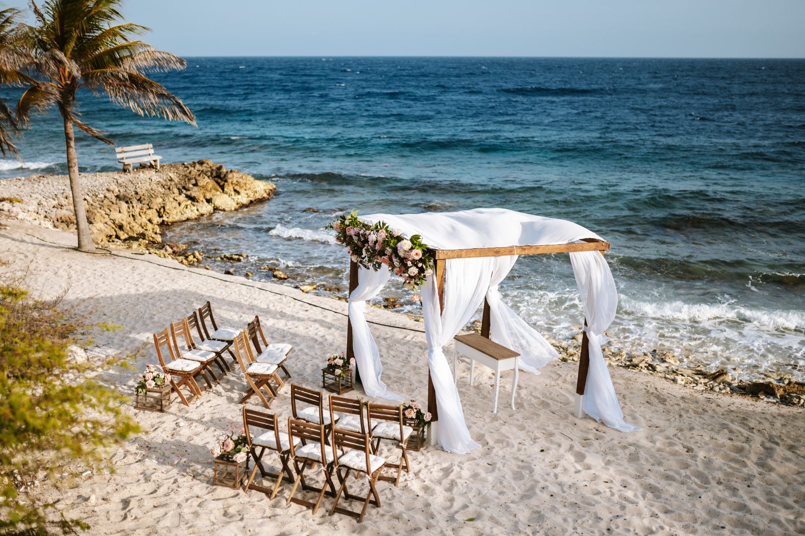 Christine and Jesse are getting married under a floral-adorned arch by the beach at a private villa in Curaçao, with chairs arranged for guests