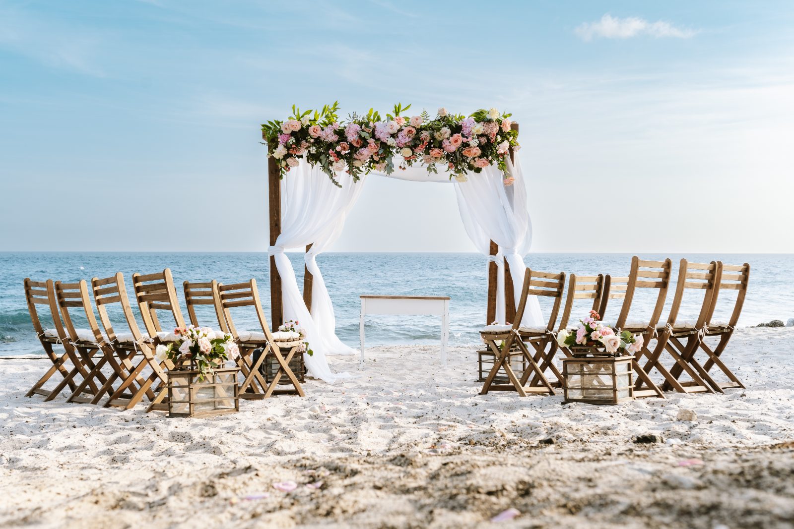 Christine and Jesse are getting married at a beachside ceremony setup with floral decor, chairs arranged on the sand, and the ocean in the background