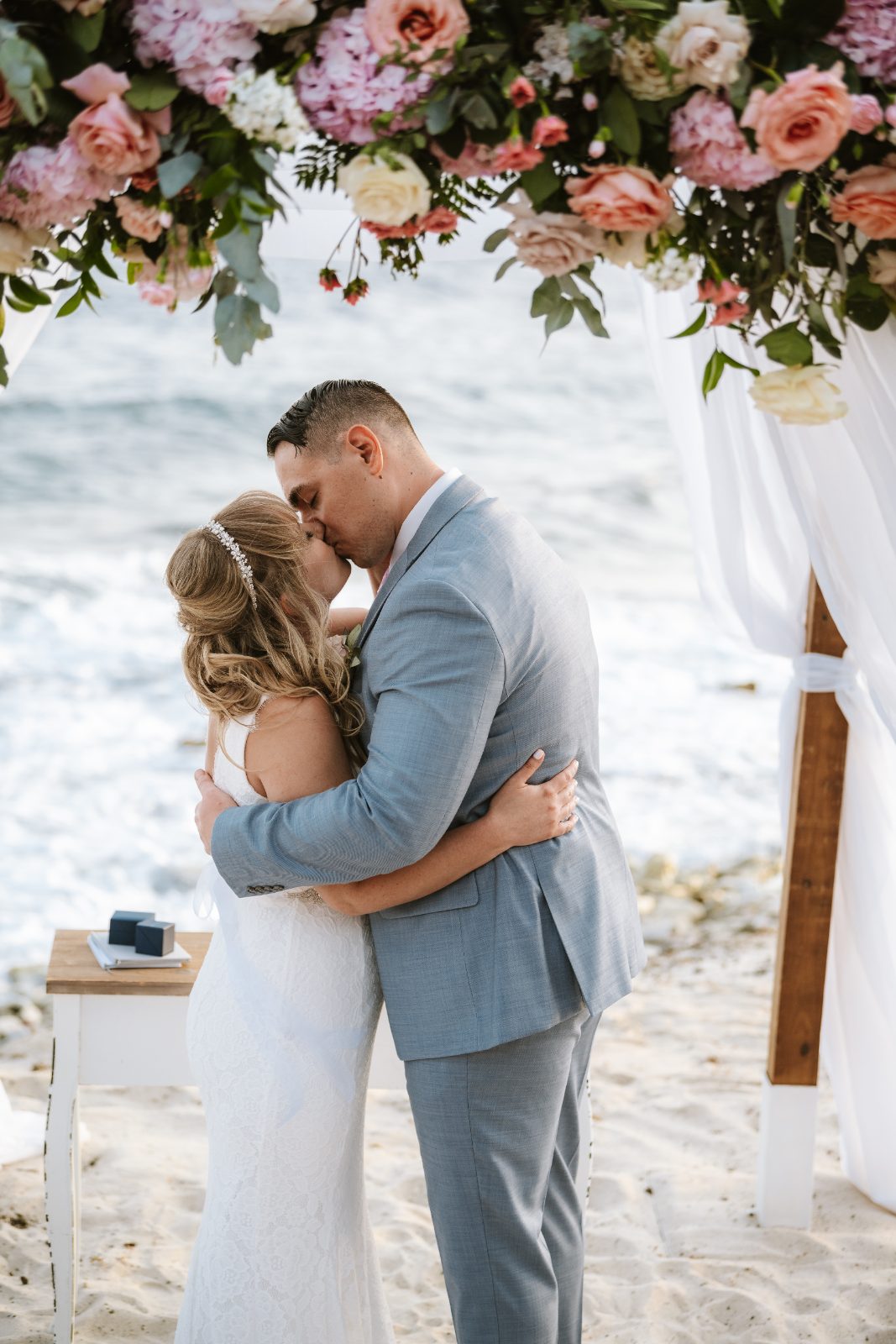 Christine and Jesse are sharing a kiss under floral decorations at their wedding ceremony on the beach in Curaçao