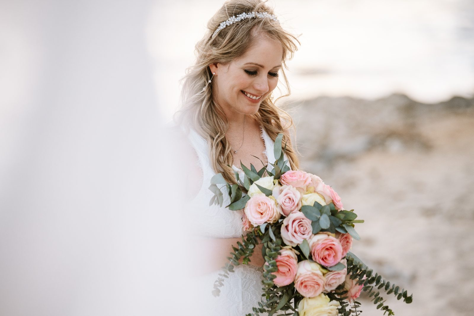 Christine stands on a beach at a private villa in Curaçao, holding a bouquet of roses and smiling