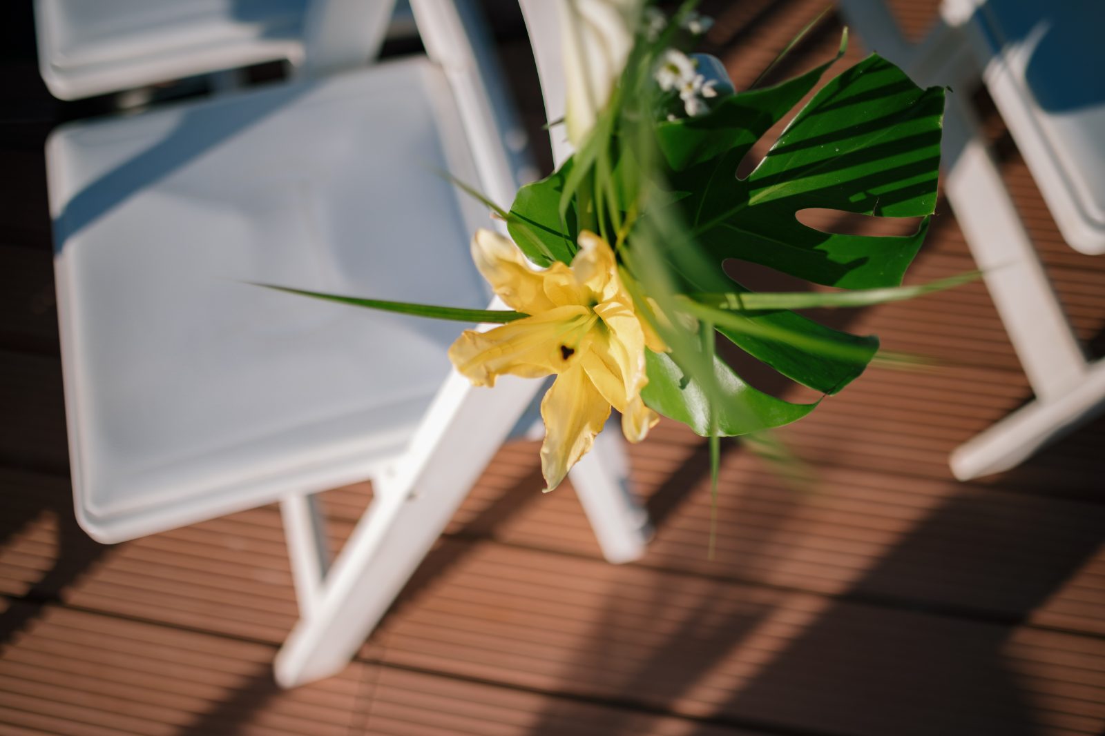 Erica and Derek's wedding at Avila Beach Hotel features a close-up of a yellow flower arrangement next to white chairs on a wooden deck