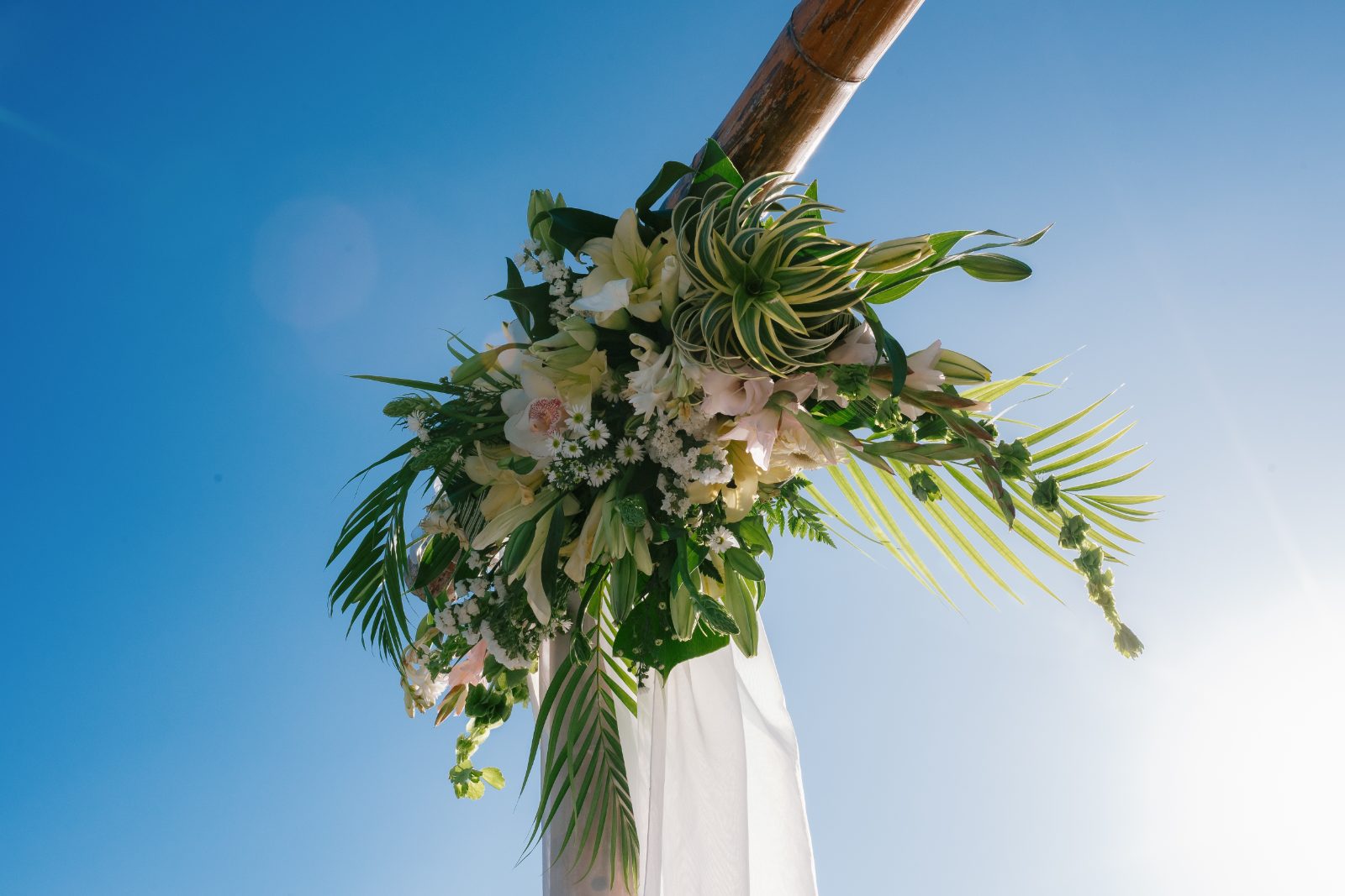 Erica and Derek are getting married at the Avila Beach Hotel in Curaçao, with a floral arrangement prominently displayed against a clear blue sky