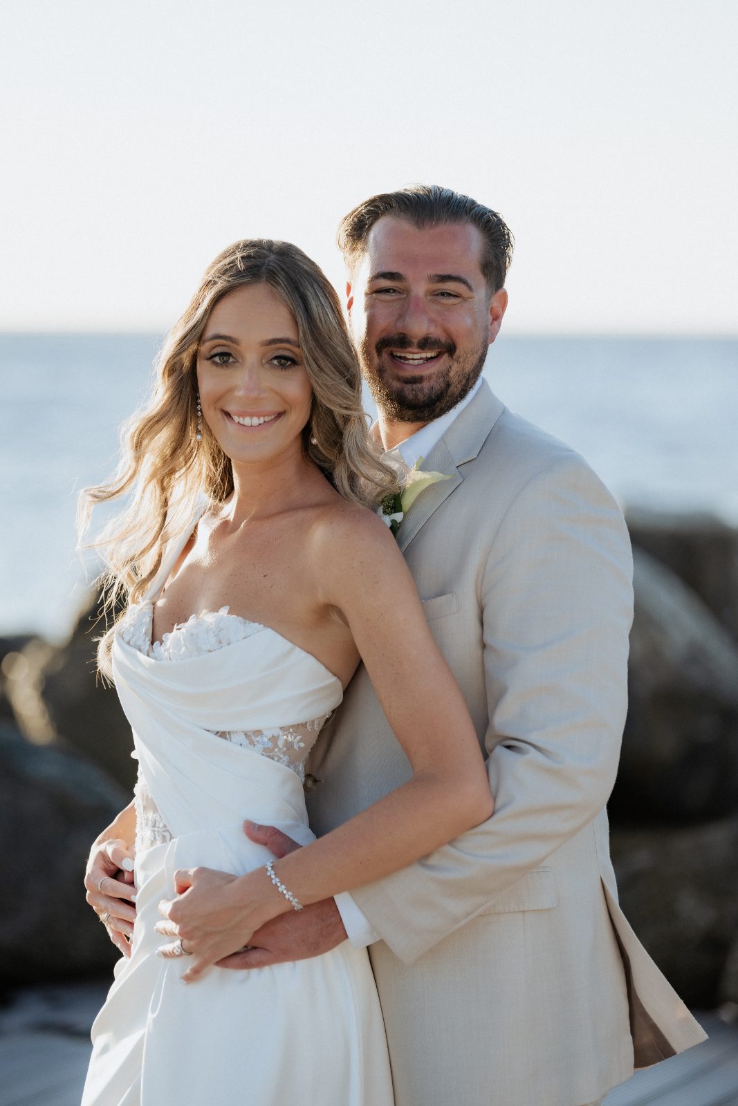 Erica and Derek pose together on a beach at the Avila Beach Hotel in Curaçao, with the ocean visible behind them