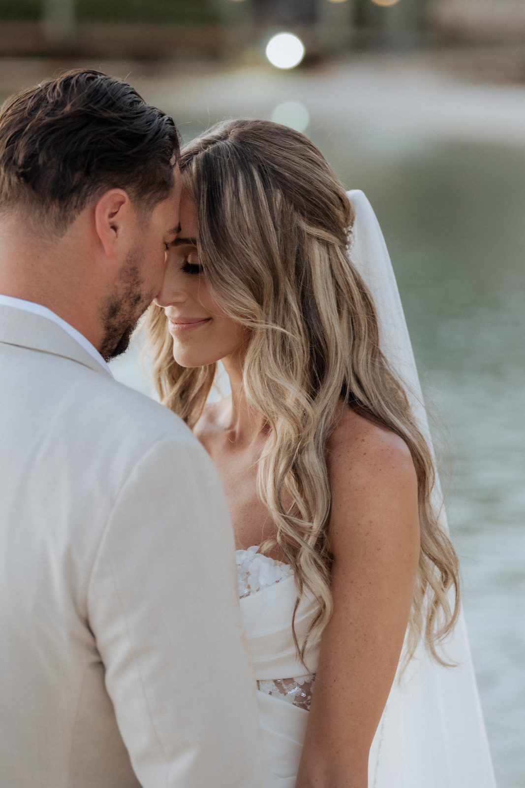 Erica and Derek stand close together at Avila Beach Hotel in Curaçao, with their foreheads touching near water