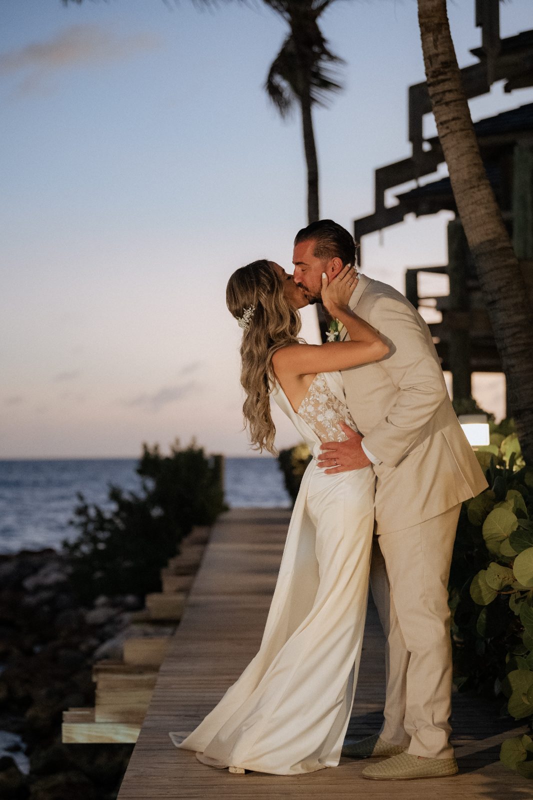 Erica and Derek kiss on a wooden path at the Avila Beach Hotel in Curaçao during their wedding