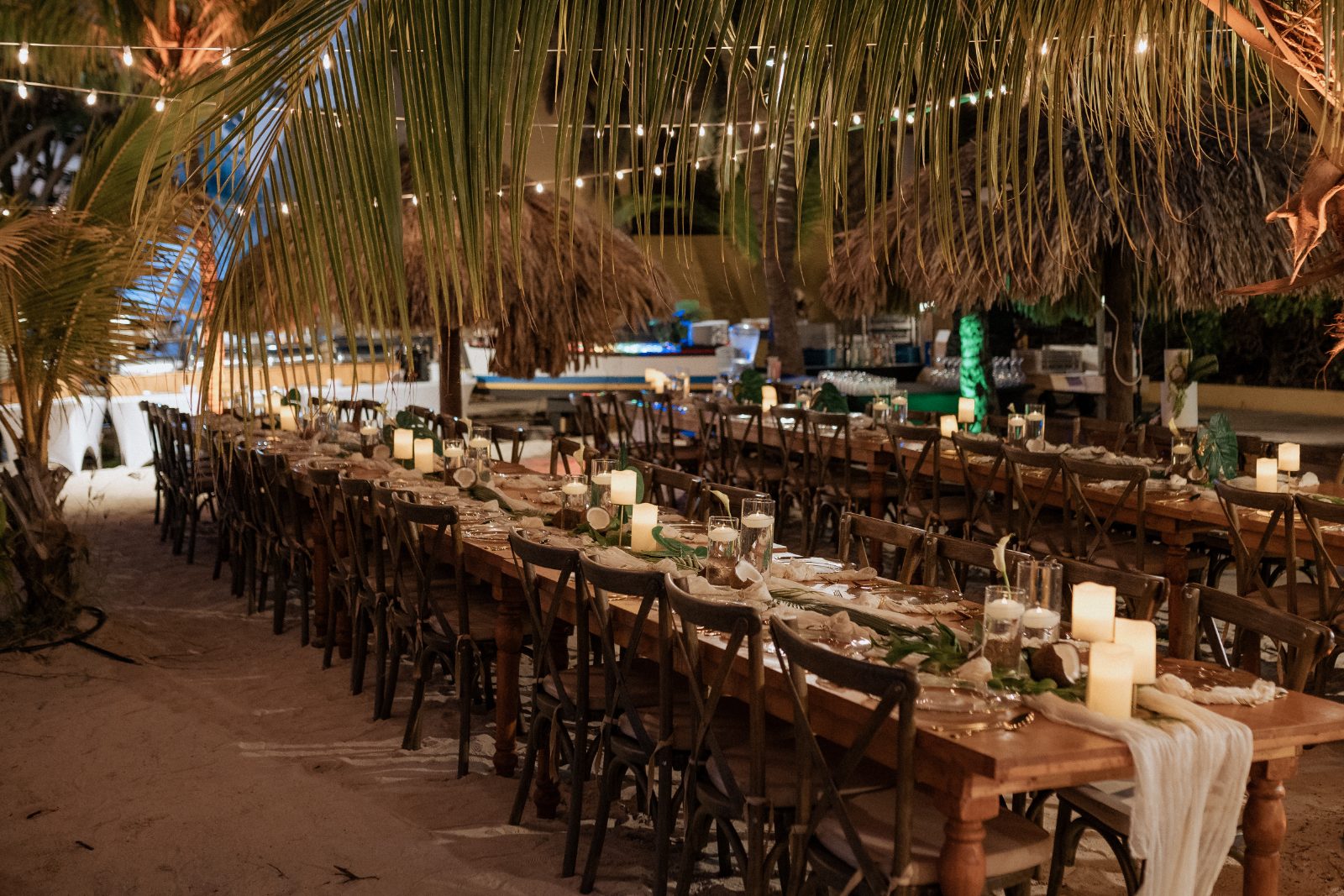 Guests are seated at long wooden tables decorated with candles and greenery in a beachside setting at Avila Beach Hotel in Curaçao