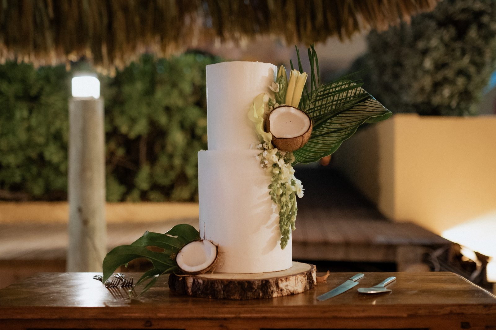 Erica and Derek's wedding cake is displayed on a wooden table at the Avila Beach Hotel in Curaçao, with tropical decorations and fresh coconut