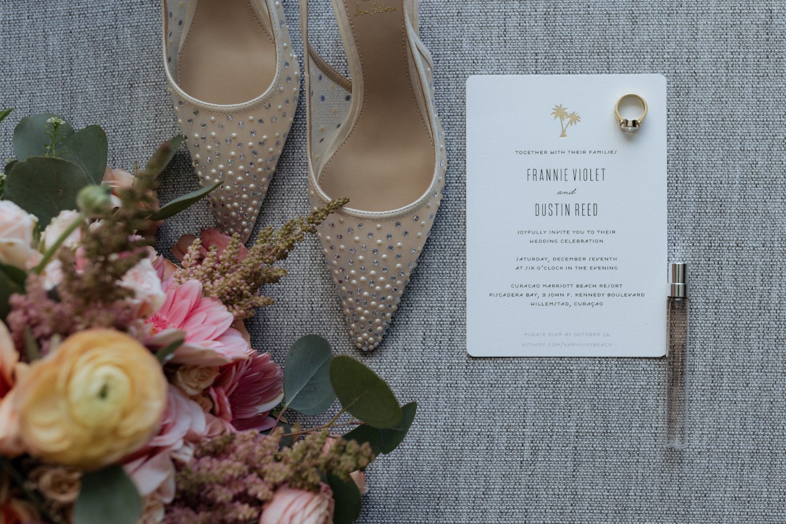 Frannie and Dustin's flatlay at Curaçao Marriott Beach Resort features wedding shoes, a floral bouquet, an invitation, and a ring on a textured surface