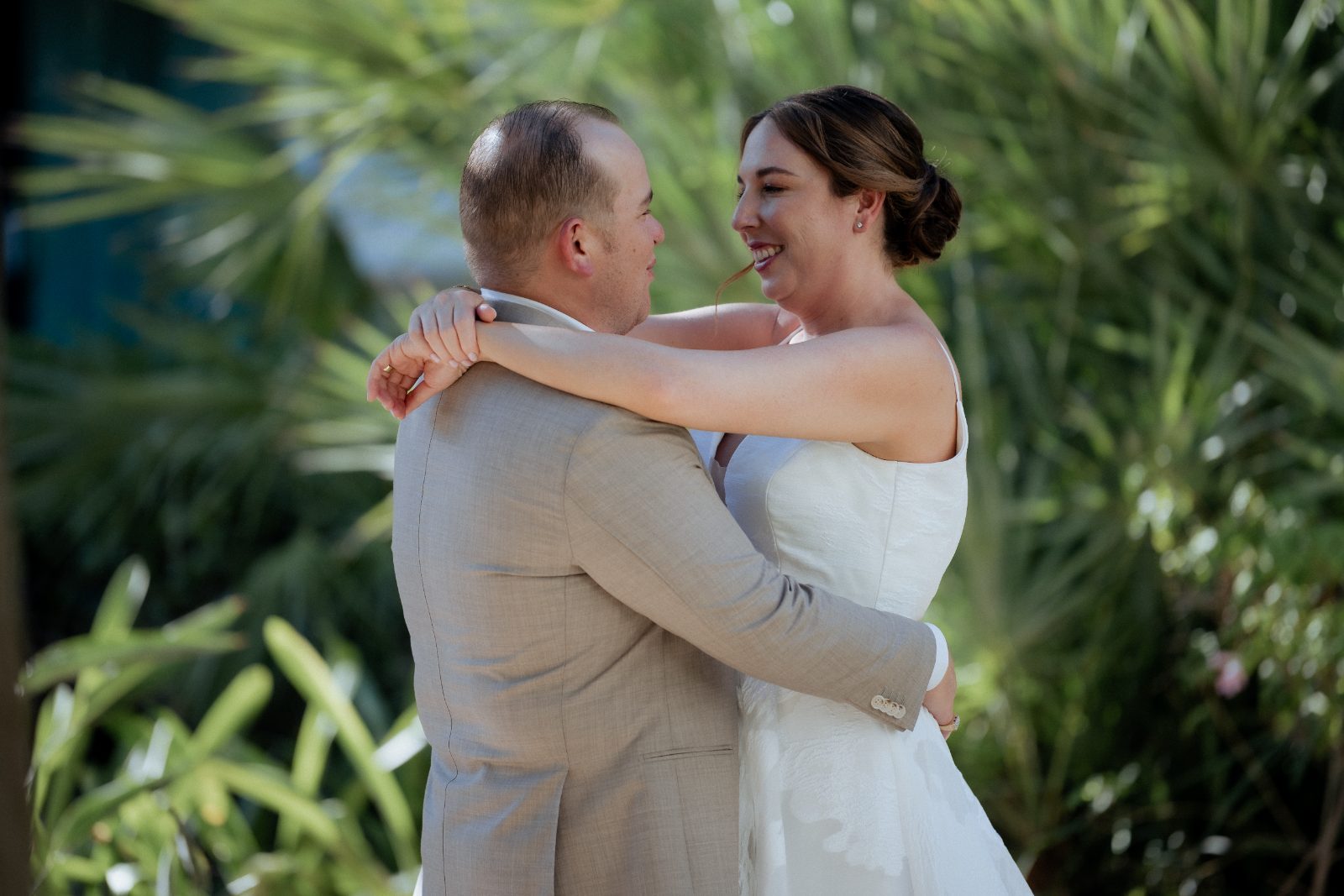 Frannie and Dustin embrace while smiling at each other in front of lush greenery at the Curaçao Marriott Beach Resort during their first look