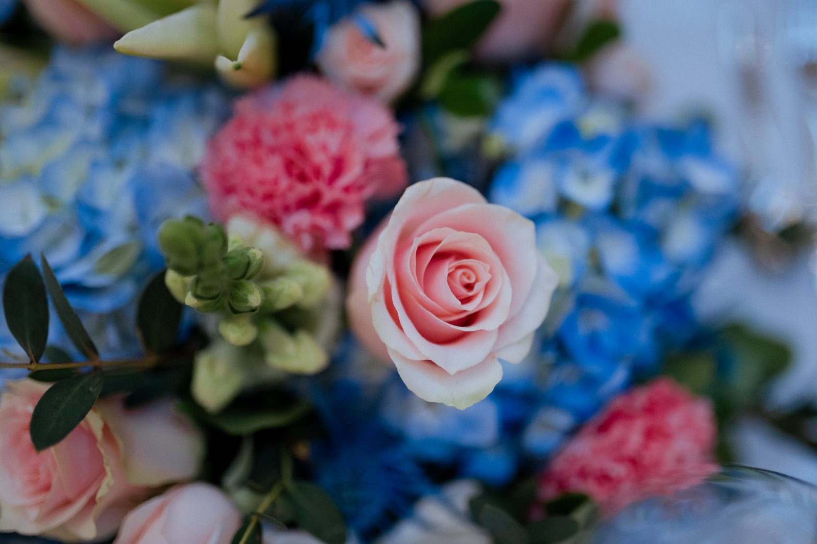 Frannie and Dustin's centerpiece at Shabbat dinner features pink roses, blue and pink flowers, and greenery, set at the Curaçao Marriott Beach Resort