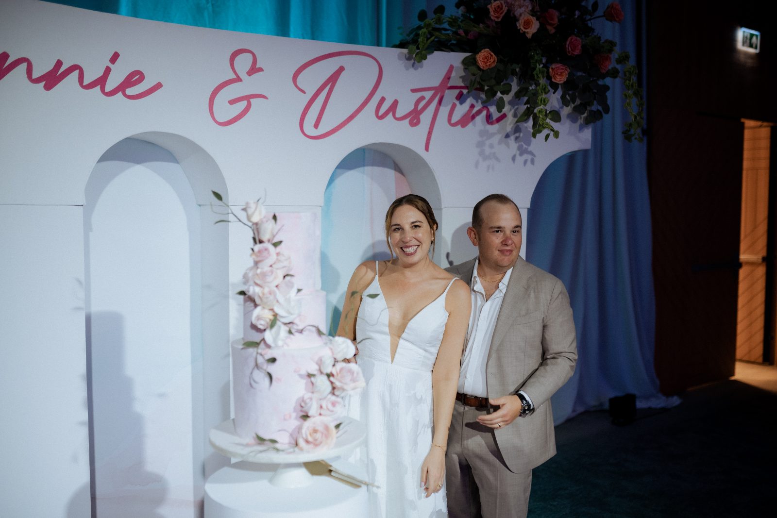Frannie and Dustin cake cutting at the Curaçao Marriott Beach Resort, smiling in front of a floral backdrop