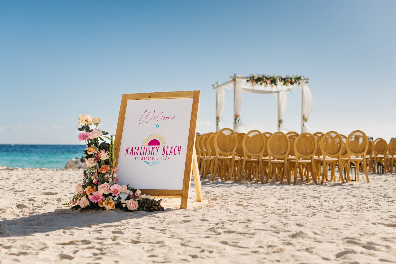 The wedding ceremony at Curaçao Marriott Beach Resort features a decorative welcome sign and rows of chairs set up on the beach near the ocean