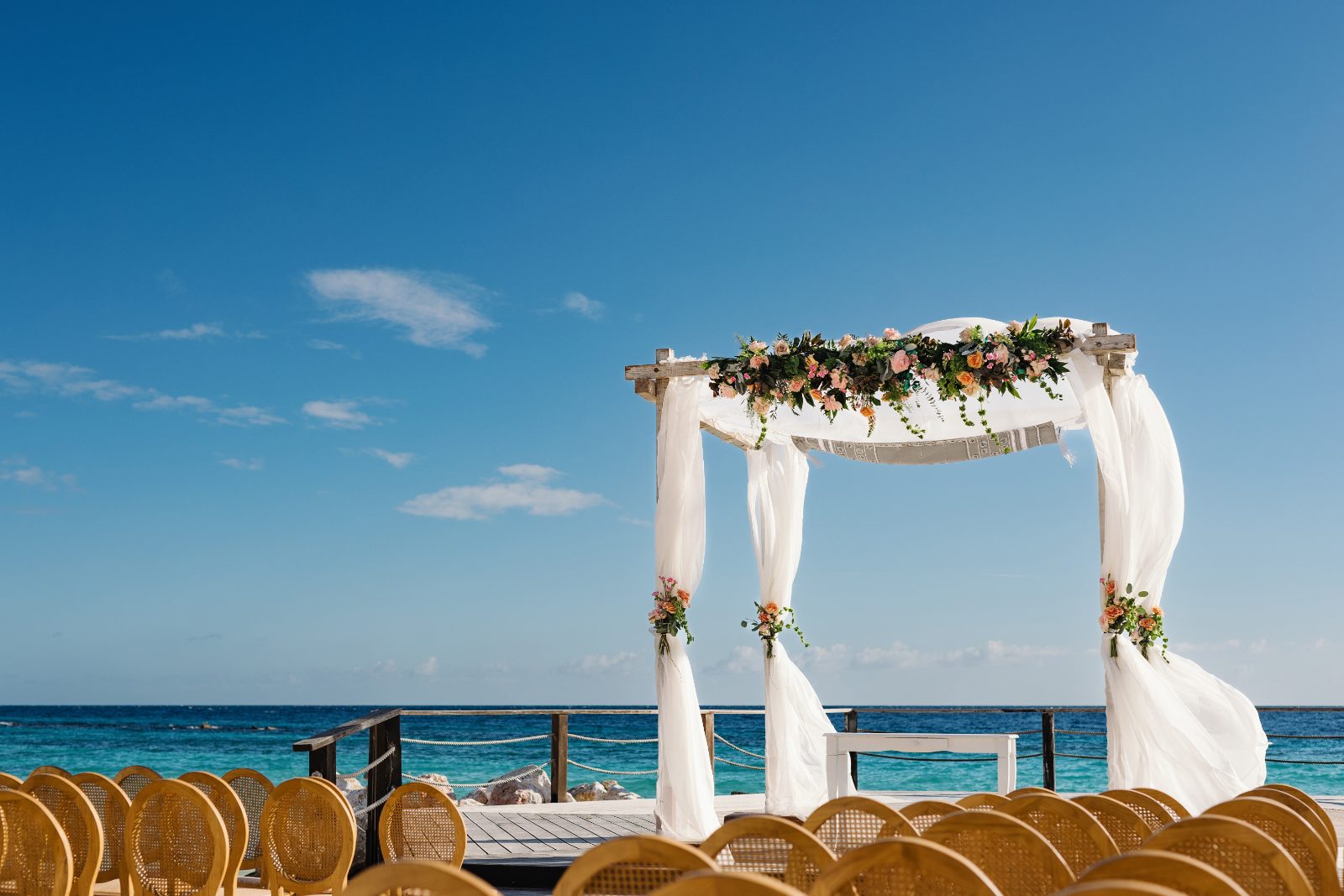 Frannie and Dustin's wedding is set at Curaçao Marriott Beach Resort, featuring an outdoor altar decorated with flowers and chairs facing the ocean