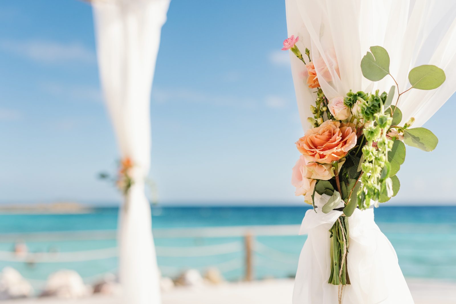 Frannie and Dustin are having their wedding ceremony at the Curaçao Marriott Beach Resort, overlooking the ocean with floral decorations in the foreground