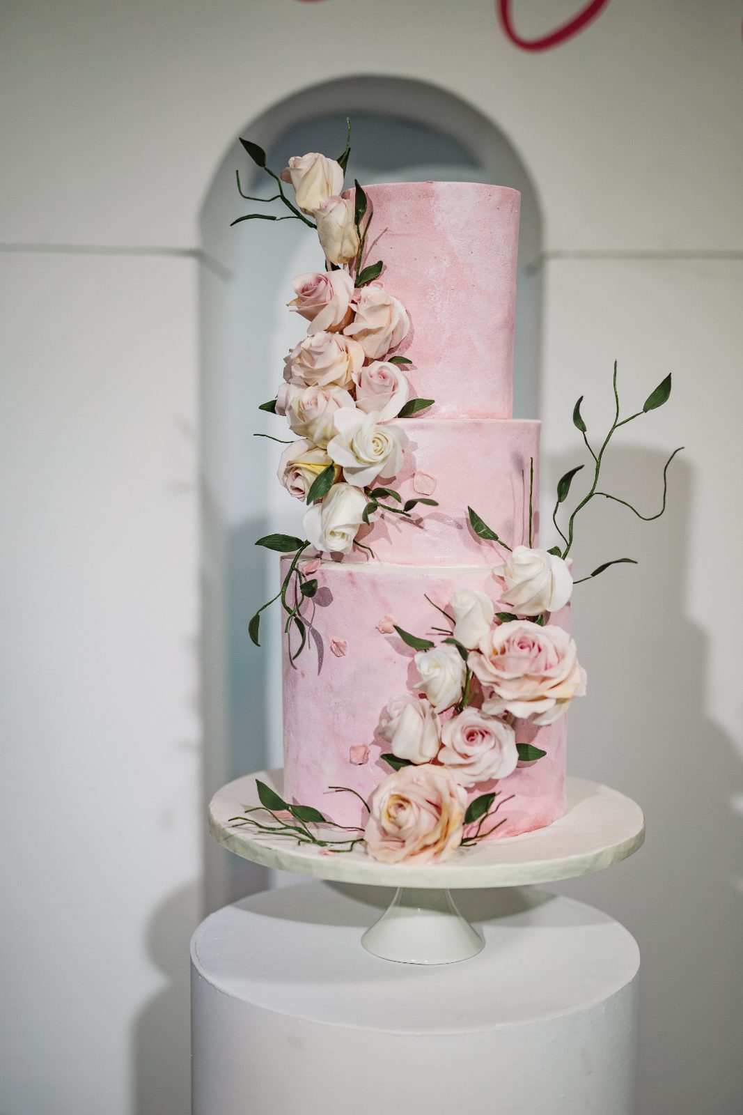 Frannie and Dustin's wedding cake, a three-tiered pink design adorned with white and pink roses, is displayed at the Curaçao Marriott Beach Resort