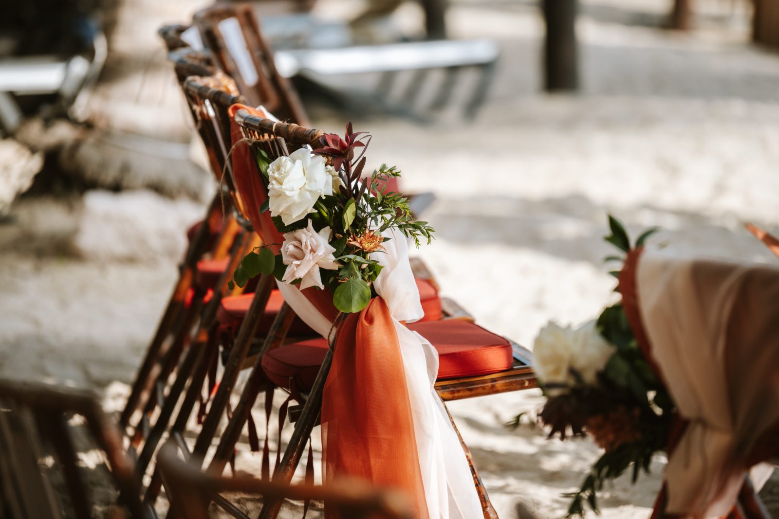 Gaëlle and Jeroen's wedding details are set at Avila Beach Hotel in Curaçao, featuring decorated chairs with flowers and fabric trim for the ceremony