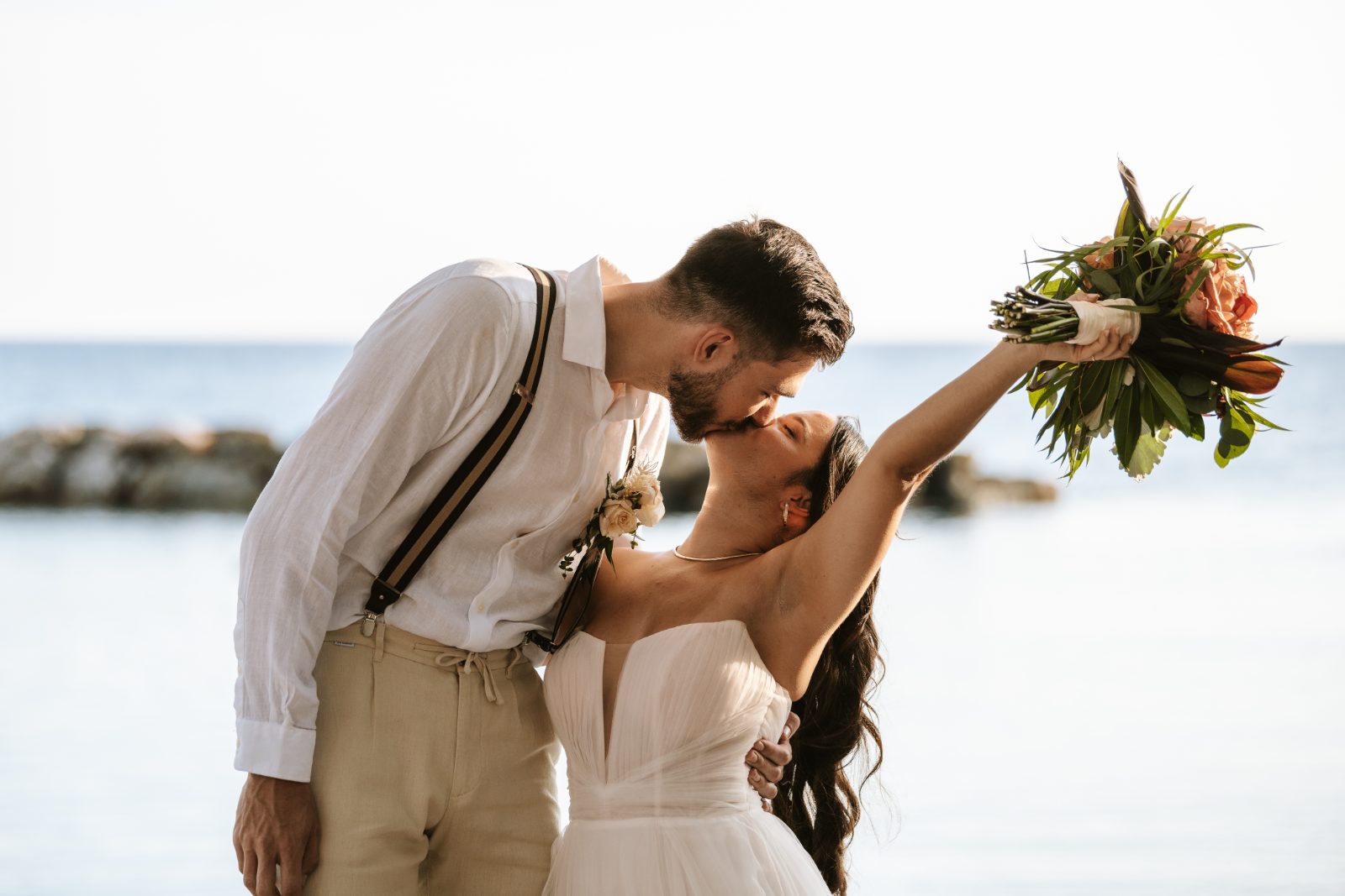 Gaëlle and Jeroen kiss near the water at Avila Beach Hotel in Curaçao, with Gaëlle holding a bouquet above her head