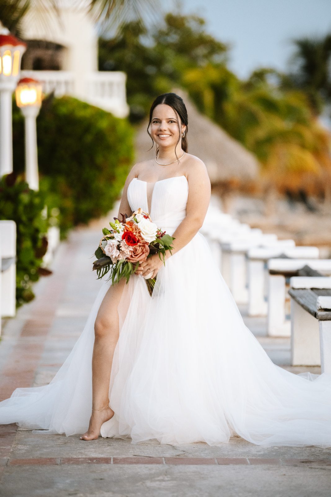 Gaëlle in a white wedding dress holds a bouquet while standing barefoot on a walkway at Avila Beach Hotel in Curaçao
