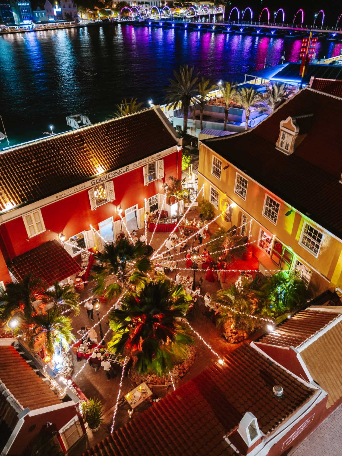 Gaëlle and Jeroen's wedding takes place at De Gouverneur in Curaçao, with decorated surroundings, a waterfront view, and guests seated around the venue