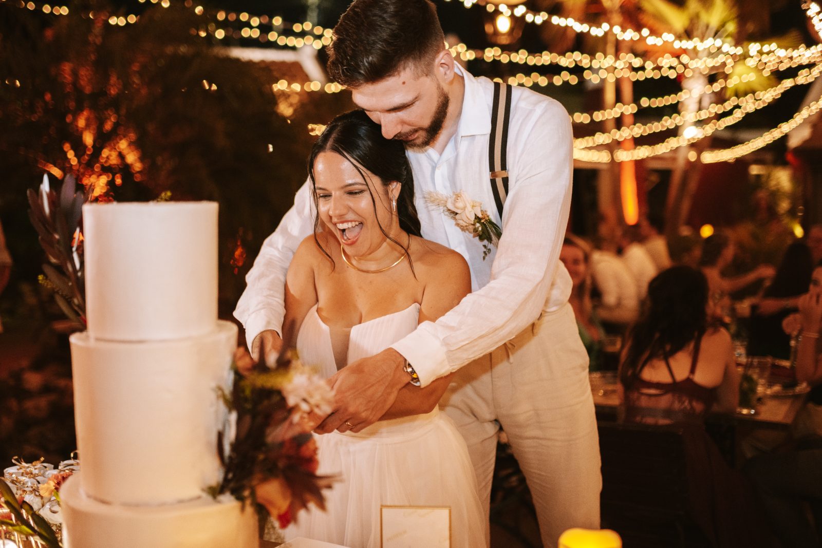Gaëlle and Jeroen are cutting their wedding cake at a reception with string lights at Avila Beach Hotel in Curaçao
