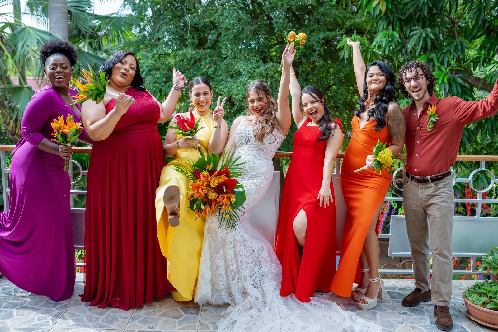 Ghislaine and Kevin celebrate their wedding in a private garden in Curaçao, surrounded by six joyful friends in colorful dresses, holding flowers and posing
