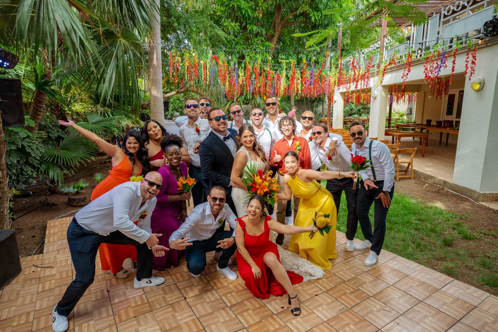 Ghislaine and Kevin celebrate their wedding in a private garden in Curaçao, surrounded by friends and family in bright outfits holding bouquets
