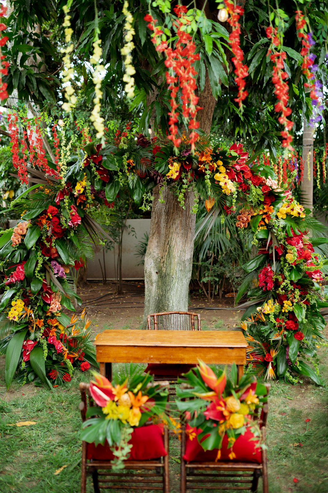Ghislaine and Kevin are set to be married in a colorful floral arch amidst a private garden in Curaçao, with a wooden table and decorated chairs