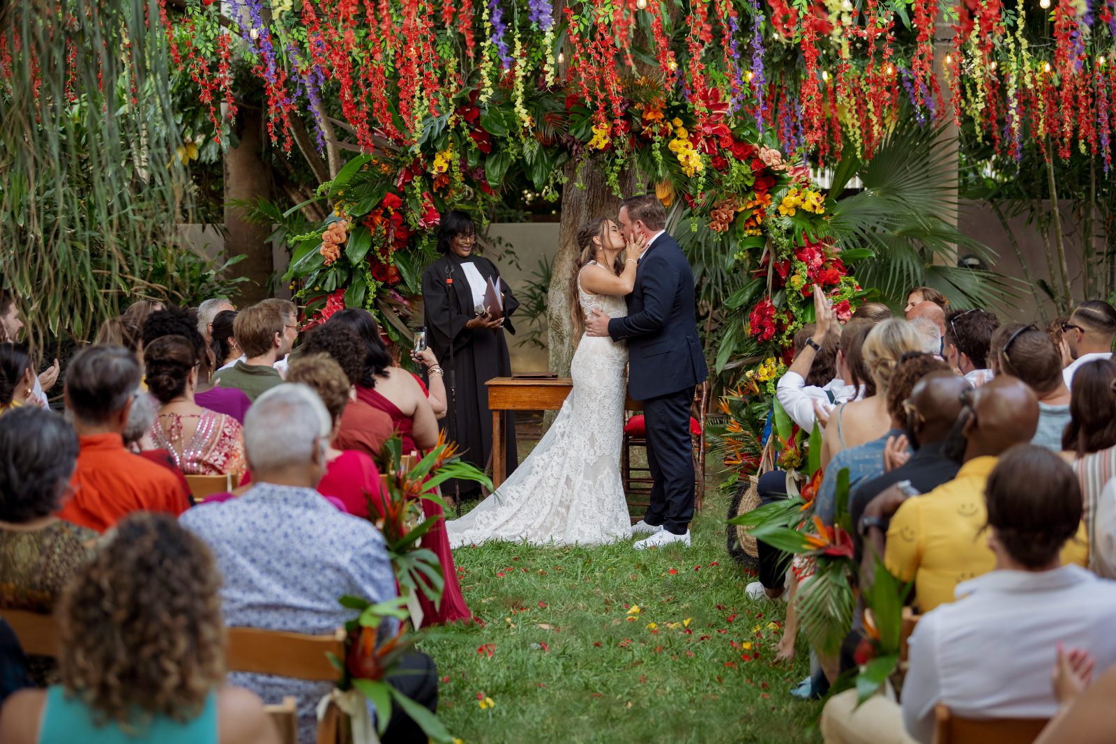Ghislaine and Kevin are exchanging vows in a private garden in Curaçao, surrounded by guests and a floral backdrop