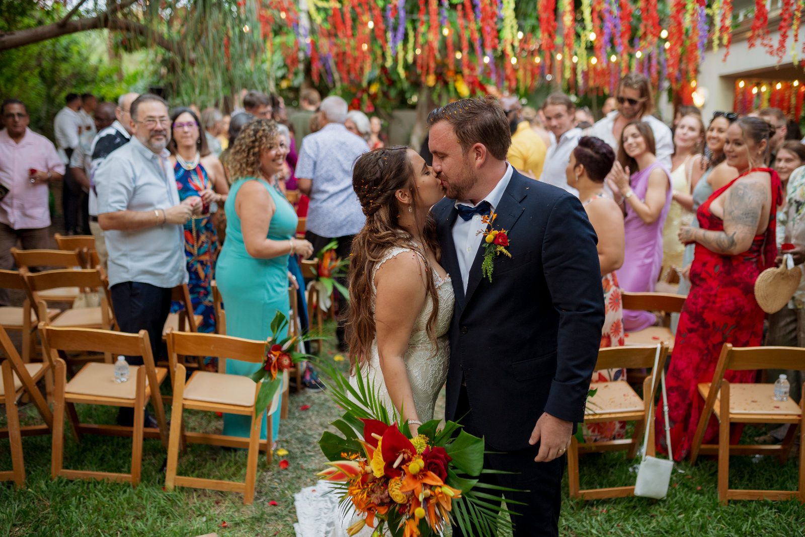 Ghislaine and Kevin are kissing during their wedding ceremony in a private garden in Curaçao, surrounded by guests celebrating