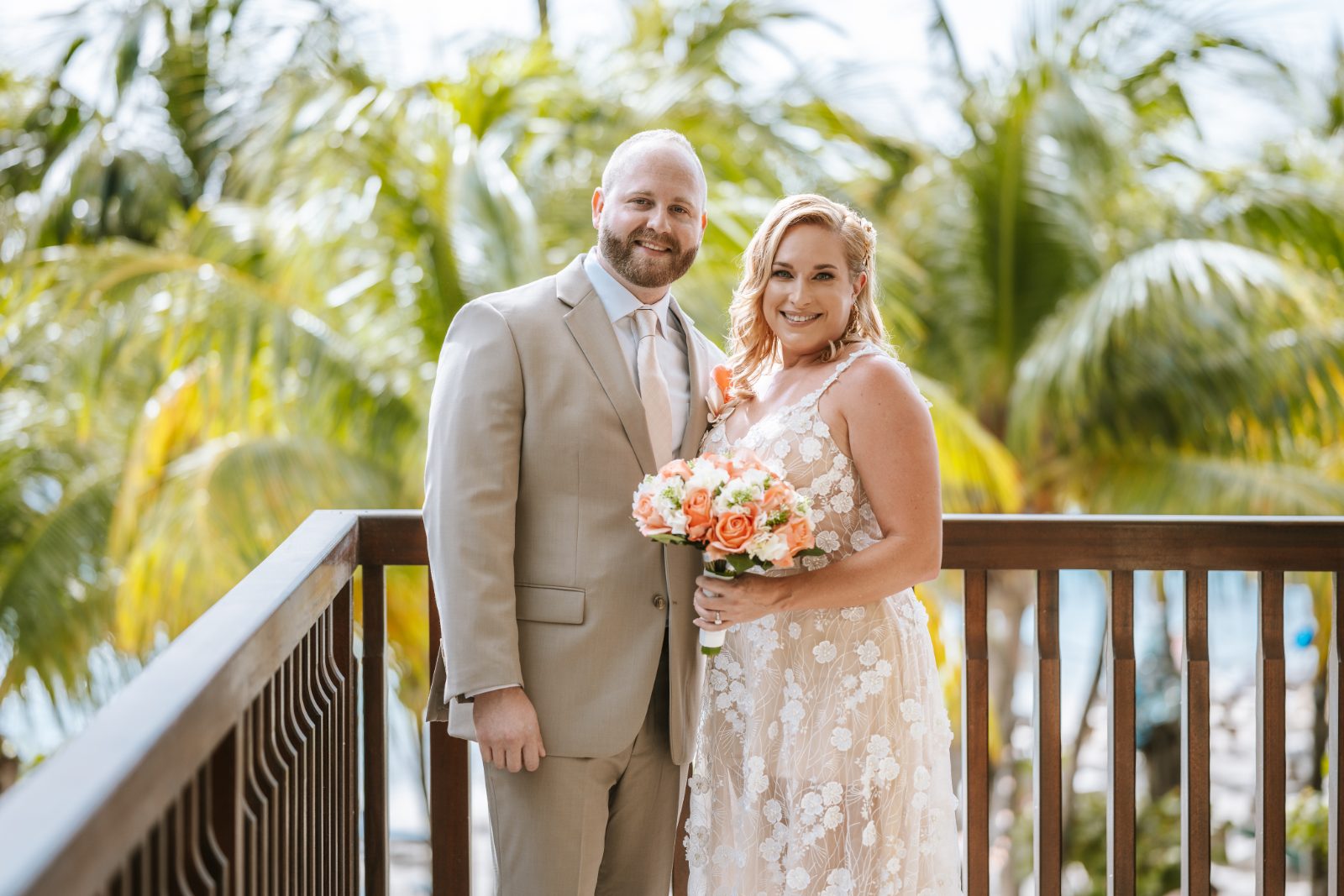 Jennifer and Weston stand together on a balcony at Karakter, Curaçao, surrounded by palm trees, holding a bouquet of flowers