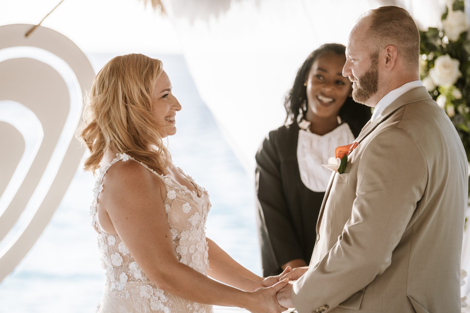Jennifer and Weston hold hands during their wedding ceremony at Karakter in Curaçao, while an officiant stands nearby